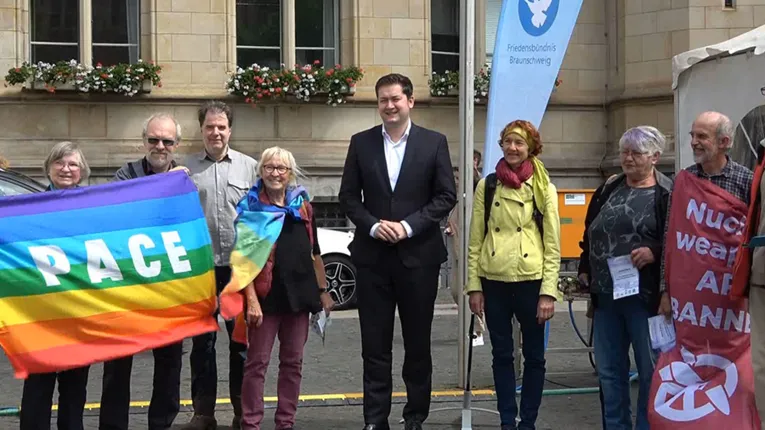 M&auml;nner und Frauen stehen vor dem Rathaus in Braunschweig mit der Nuklear-Ban-Flagge.